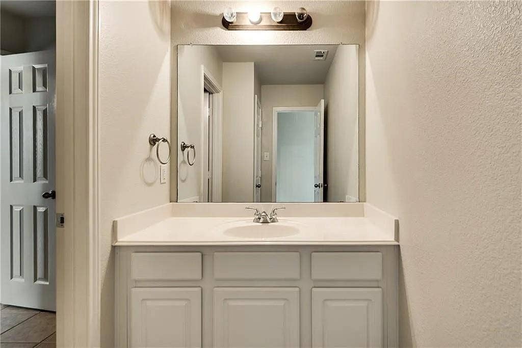 9304 Regal Oaks Drive, McKinney, TX 75072 Vanity featuring a white countertop with an integrated sink, a large wall-mounted mirror, and a three-light fixture