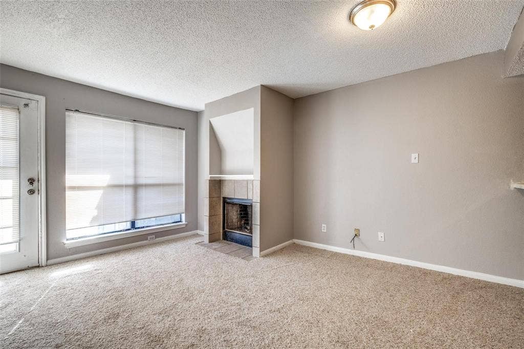 6108 Abrams Road, #118, Dallas, TX 75231 Neutral tone wall paint, textured ceiling, built-in fireplace with tile surround, window with blinds, and light carpet flooring
