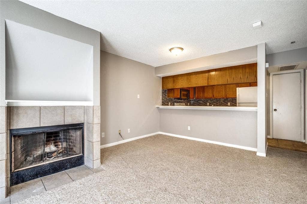 6108 Abrams Road, #118, Dallas, TX 75231 Carpeted living area with a tile-surround fireplace and built-in mantel