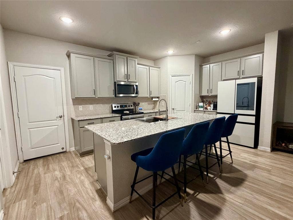 2812 Appaloosa Lane, Mesquite, TX 75150 Kitchen featuring a large island with stone countertop, stainless steel appliances, light-toned cabinetry, a subway tile backsplash, and wood-finish flooring