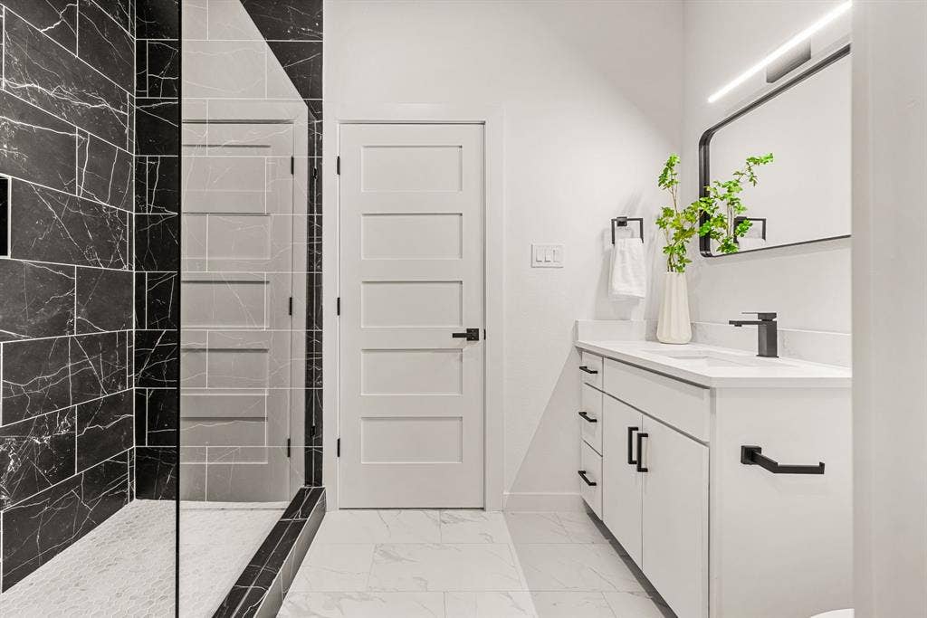 2232 Hooper Street, Dallas, TX 75215 Contemporary bathroom featuring a white vanity with matte black hardware, a black-framed mirror, a walk-in shower with black marble-style tile, and white five-panel interior doors