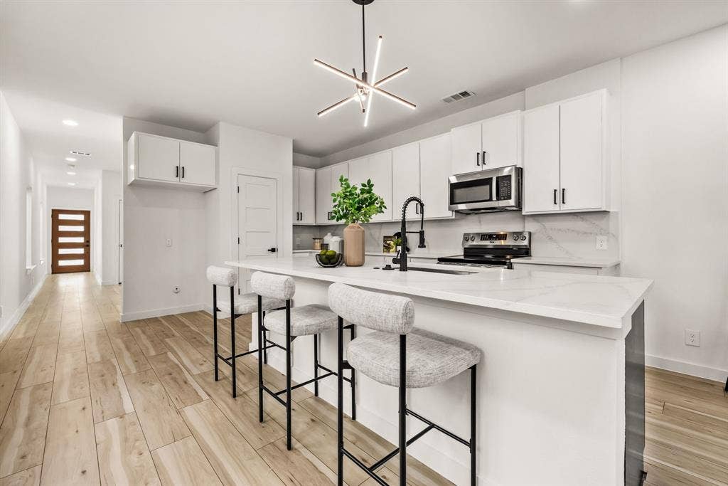 2232 Hooper Street, Dallas, TX 75215 Contemporary kitchen featuring a large island with seating, stainless steel appliances, white cabinetry, and wood-finish flooring
