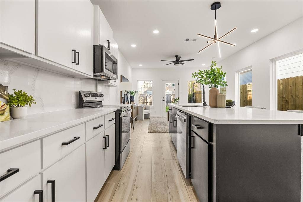 2232 Hooper Street, Dallas, TX 75215 Modern kitchen featuring white cabinetry, a large kitchen island with a white countertop, stainless steel appliances, wood-finish flooring, and recessed lighting