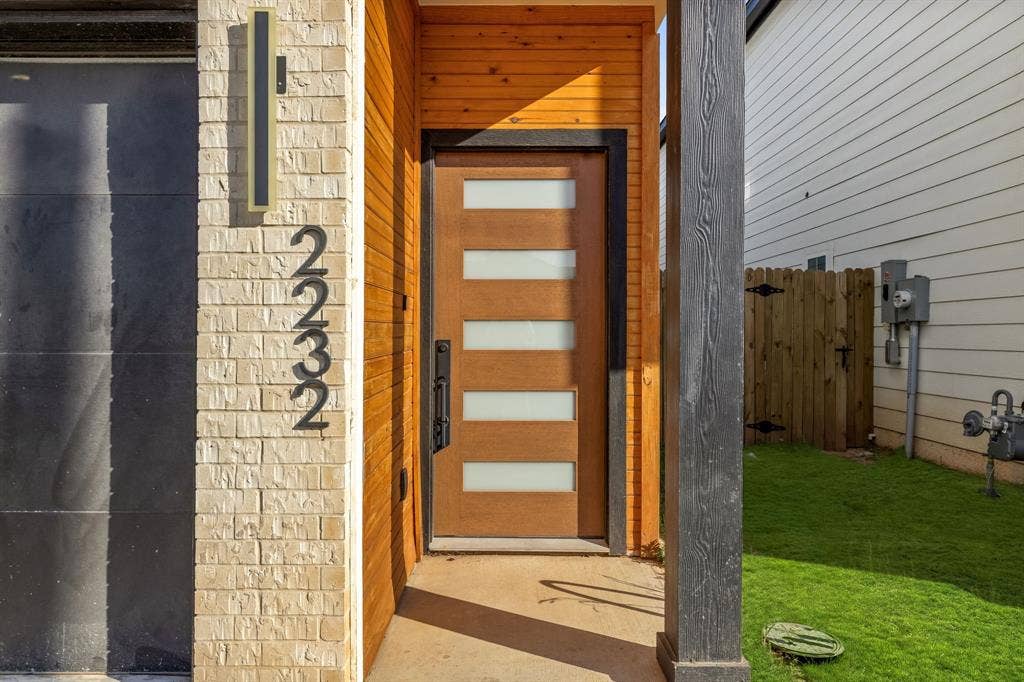2232 Hooper Street, Dallas, TX 75215 Front entry featuring a wood-finish door with frosted glass panels, brick facade, wood-plank accent wall, and a contemporary exterior sconce