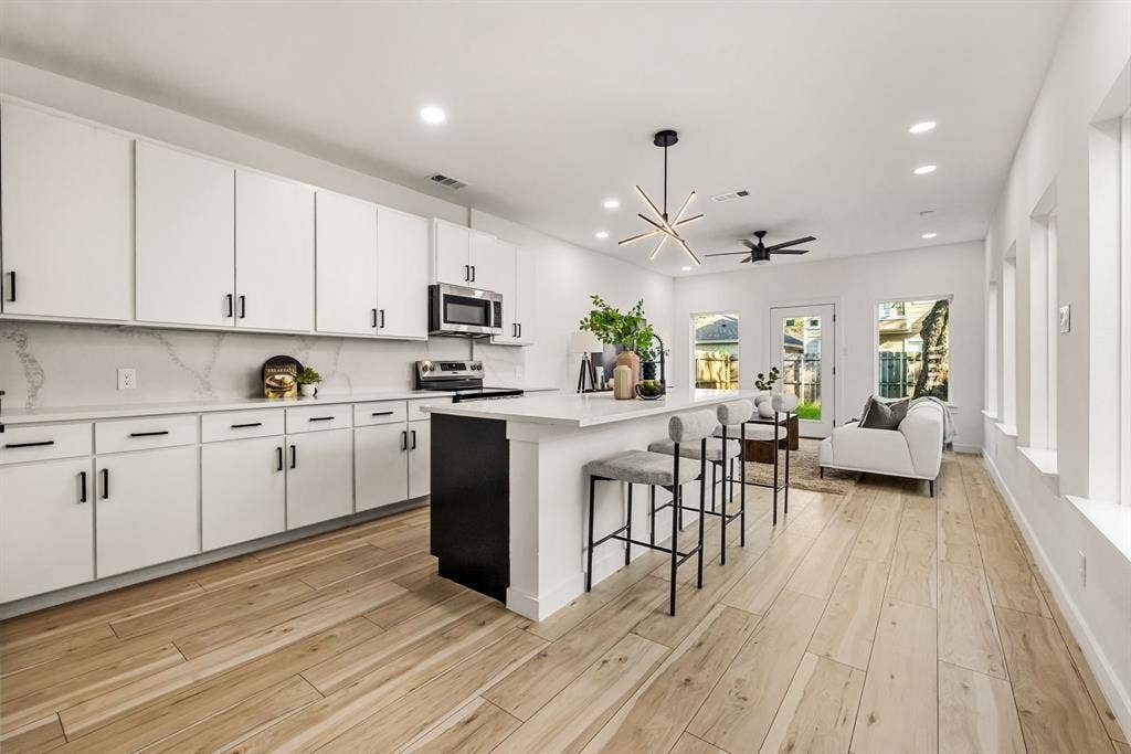 2232 Hooper Street, Dallas, TX 75215 Light wood-finish flooring, white cabinetry with dark hardware, a kitchen island with seating, recessed lighting, and a contemporary chandelier