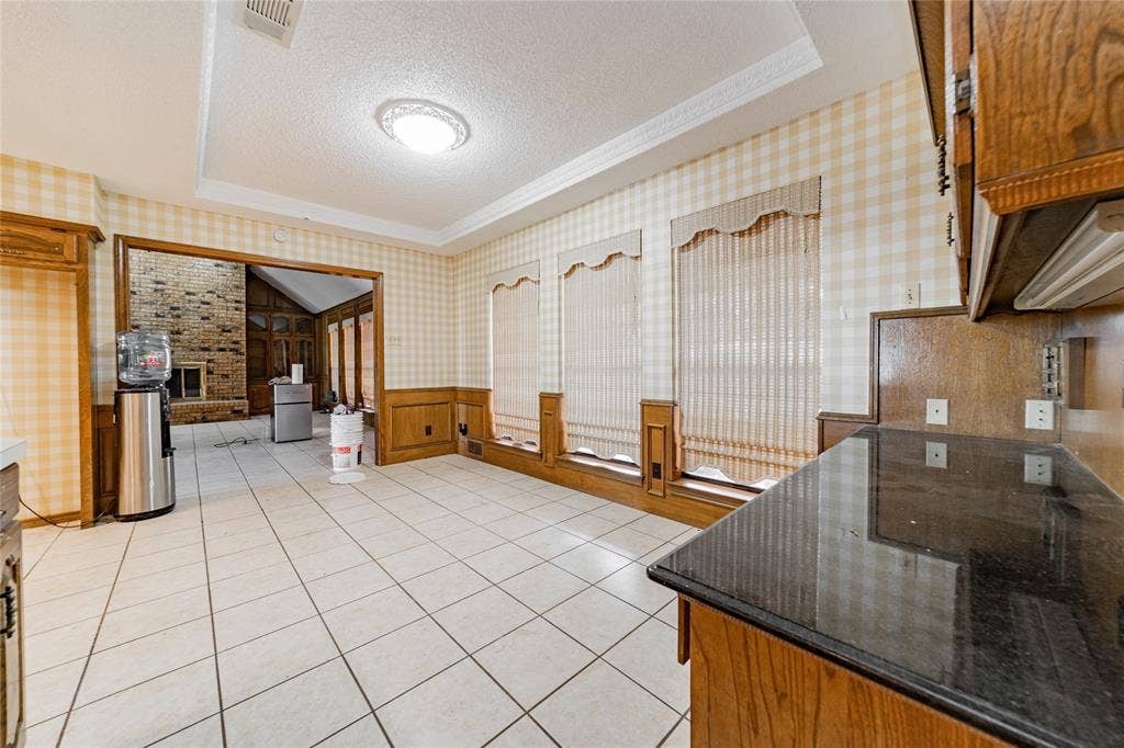 4320 Hickox Road, Rowlett, TX 75089 Tile flooring, dark countertops, wood cabinetry, wainscoting, and recessed ceiling with decorative molding