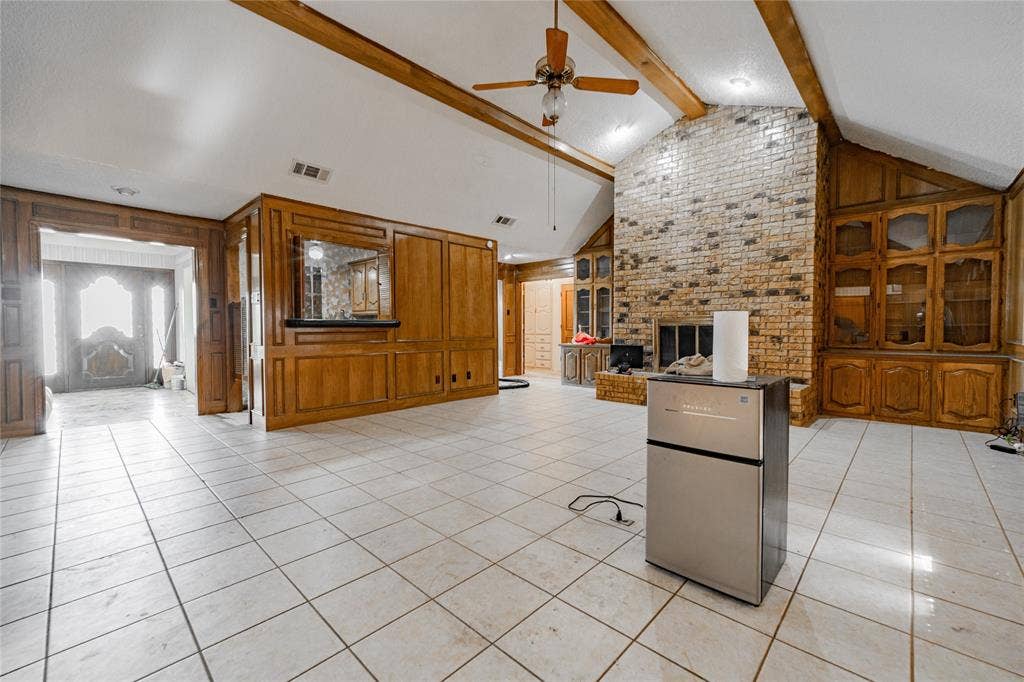 4320 Hickox Road, Rowlett, TX 75089 Vaulted ceiling with exposed wood beams, brick fireplace, built-in wood cabinetry, wood paneling, and tile flooring