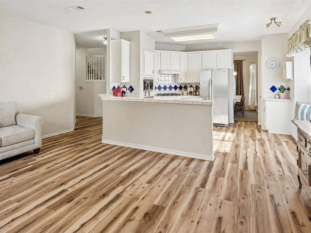 11379 Lockshire Drive, Frisco, TX 75035 Wood-finish flooring throughout, kitchen with white cabinetry, tile countertops, and stainless steel appliances