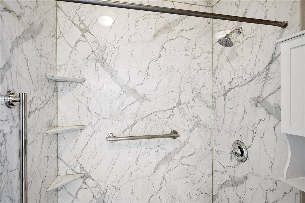 11379 Lockshire Drive, Frisco, TX 75035 White marble-patterned shower walls, polished chrome shower fixtures, corner storage shelves, and a built-in grab bar