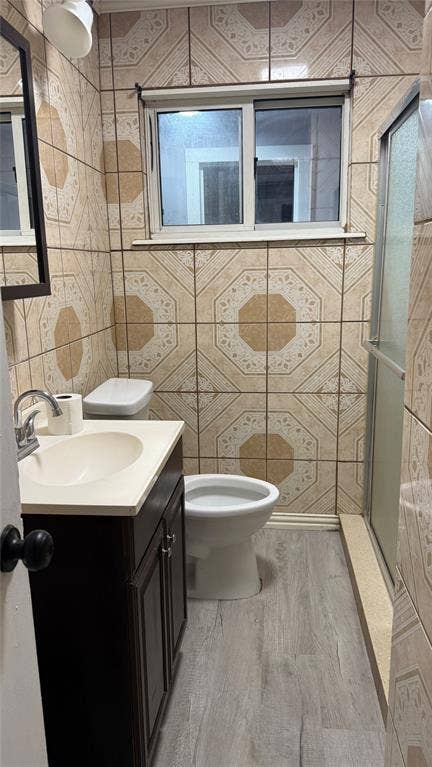 605 Biggs Terrace, Arlington, TX 76010 Patterned wall tiling, a single vanity with storage, a white toilet, and wood-finish flooring