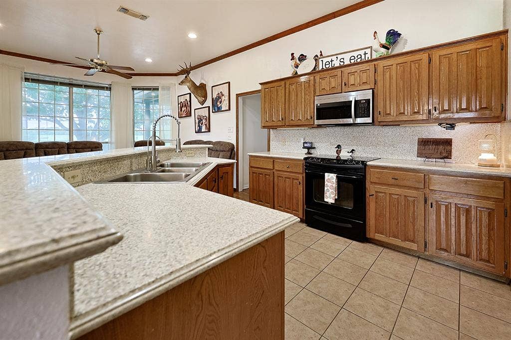 2042 County Road 1072, Greenville, TX 75401 Kitchen featuring wood cabinetry, solid-surface countertops, tile flooring, built-in microwave, and a double-basin stainless steel sink with a high-arch faucet