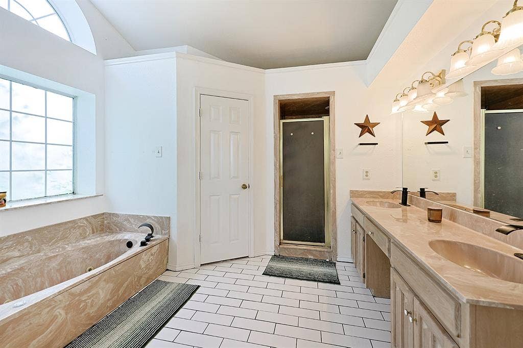 2042 County Road 1072, Greenville, TX 75401 Bathroom featuring a dual-sink vanity with stone-finish countertops, a soaking tub with matching surround, a glass-enclosed shower, and white tile flooring