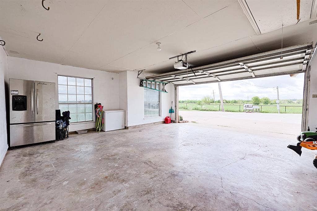 2042 County Road 1072, Greenville, TX 75401 Attached two-car garage with concrete flooring, motorized sectional garage door, multiple grid-pane windows, and high ceilings