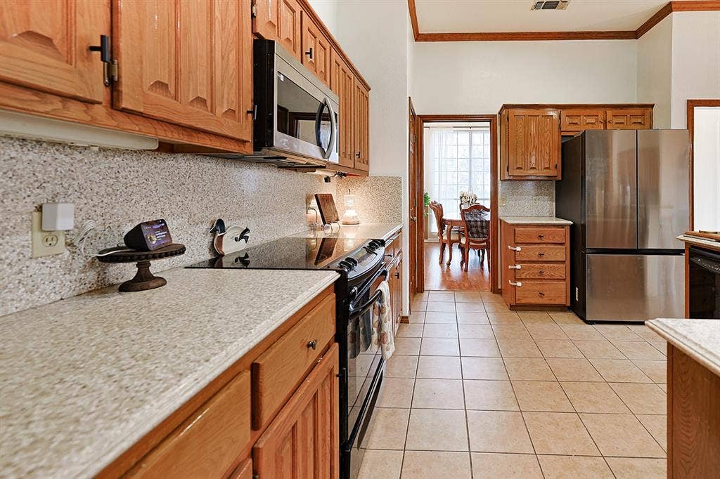 2042 County Road 1072, Greenville, TX 75401 Kitchen featuring stained wood cabinetry, stone-finish countertops, stainless steel appliances, and ceramic tile flooring