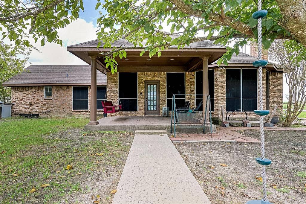 2042 County Road 1072, Greenville, TX 75401 Brick exterior featuring a covered patio with column supports, a concrete walkway, and a glass-paneled entry door