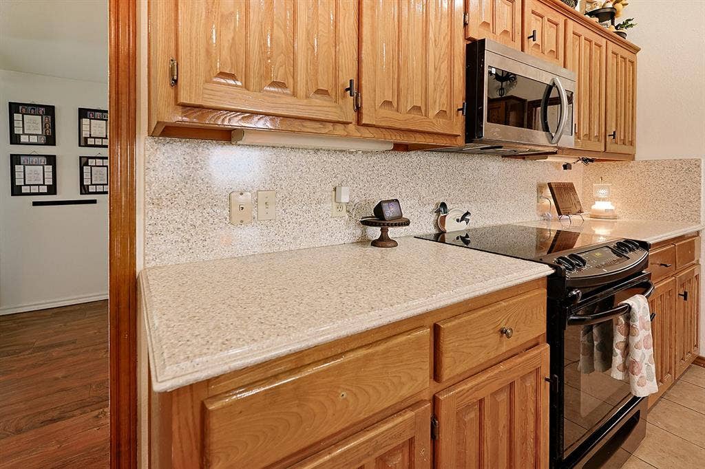 2042 County Road 1072, Greenville, TX 75401 Kitchen featuring raised-panel wood cabinetry, speckled composite countertops, a full-height matching backsplash, a built-in stainless steel microwave, and a black glass-top range
