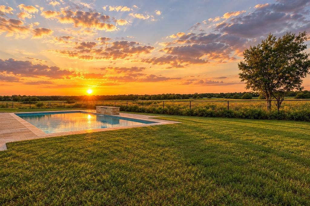 2042 County Road 1072, Greenville, TX 75401 In-ground swimming pool featuring a stone-clad waterfall edge, paved deck, expansive lawn, and metal post fencing