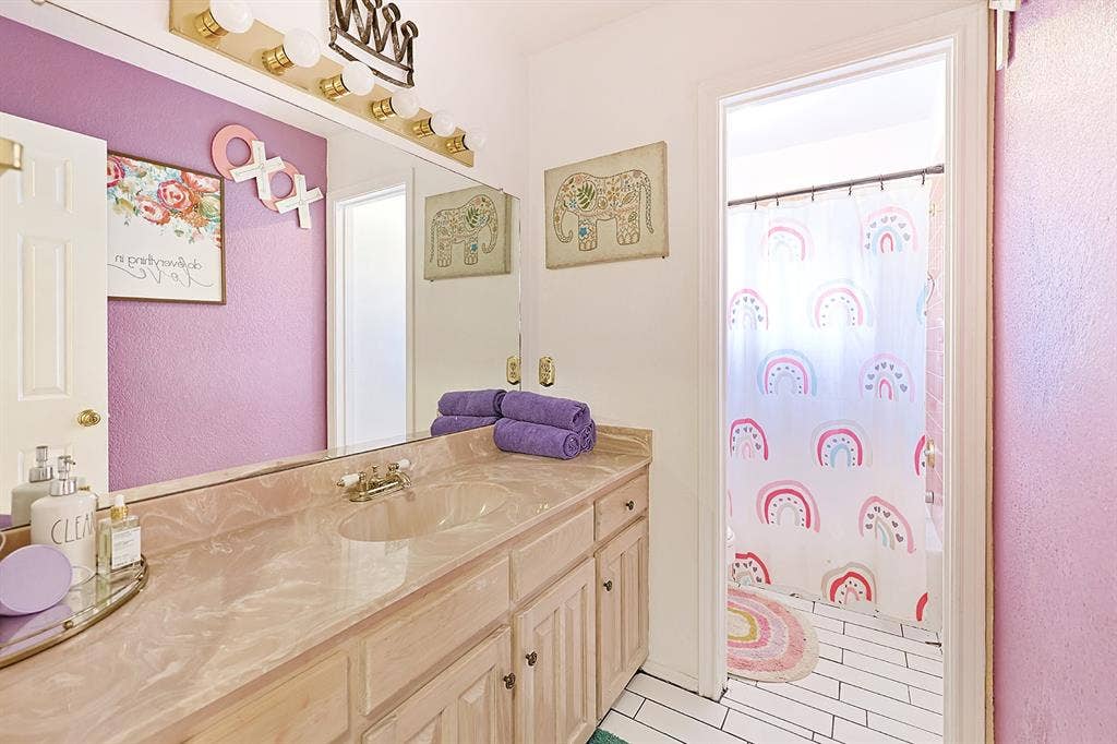 2042 County Road 1072, Greenville, TX 75401 Bathroom vanity with a stone-finish countertop, integrated basin, wood-cabinetry storage, full-width wall mirror, and overhead vanity lighting
