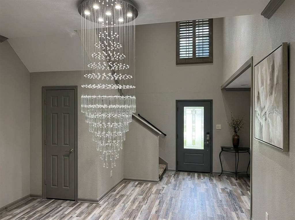 2500 Sierra Drive, McKinney, TX 75071 Two-story entryway featuring a multi-tiered crystal chandelier, wood-finish flooring, and a window with wood plantation shutters