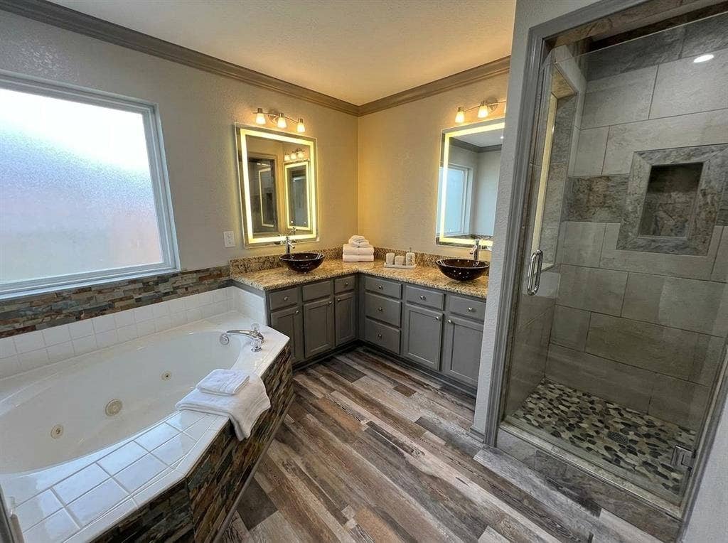 2500 Sierra Drive, McKinney, TX 75071 Dual vanity with vessel sinks, built-in soaking tub, walk-in shower with stone floor, wood-finish flooring, and frosted window