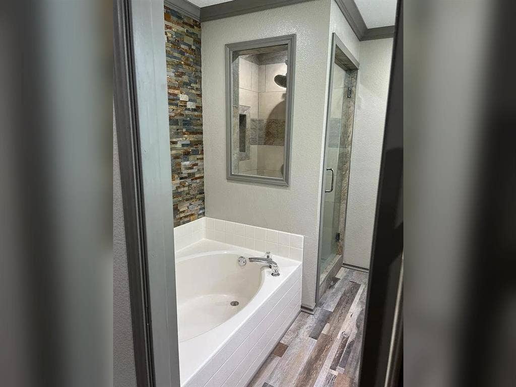 2500 Sierra Drive, McKinney, TX 75071 Corner soaking tub, stone-finish accent wall, glass-enclosed shower, wood-finish flooring, and crown molding