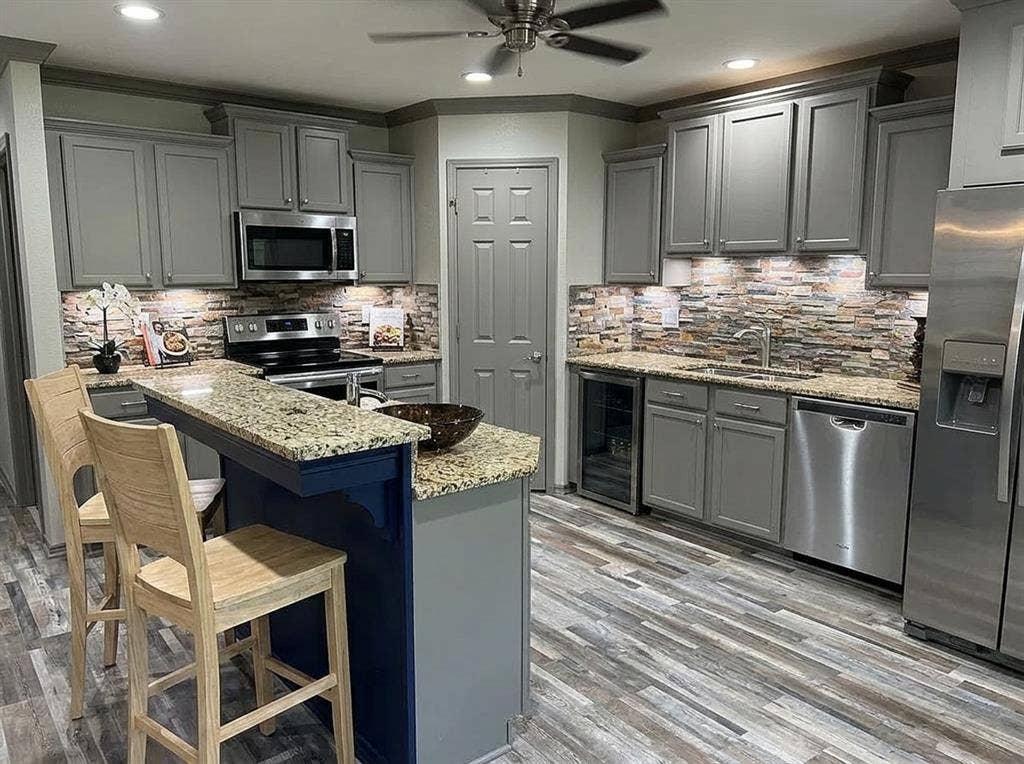 2500 Sierra Drive, McKinney, TX 75071 Kitchen featuring grey cabinetry, stainless steel appliances, a multi-tone stone backsplash, and granite countertops