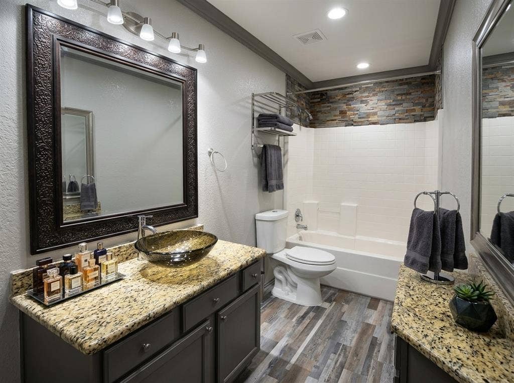 2500 Sierra Drive, McKinney, TX 75071 Wood-finish flooring, granite countertops, a vessel sink, a built-in tub with white subway tile surround, and a stacked stone accent wall