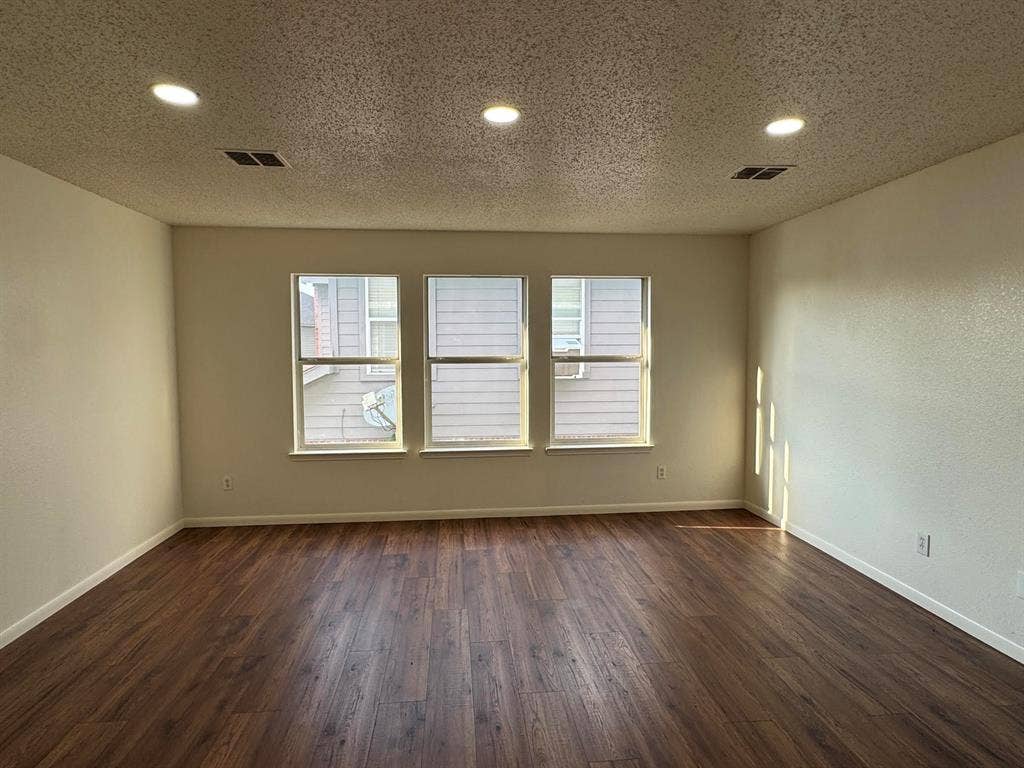 Bright interior space featuring three windows, recessed ceiling lighting, wood-finish flooring, and crisp white walls