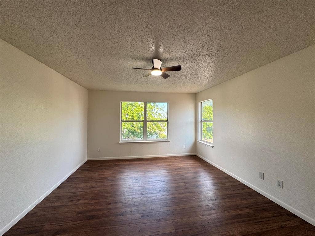 Spacious room featuring wood-finish flooring, light-toned walls, and multiple windows