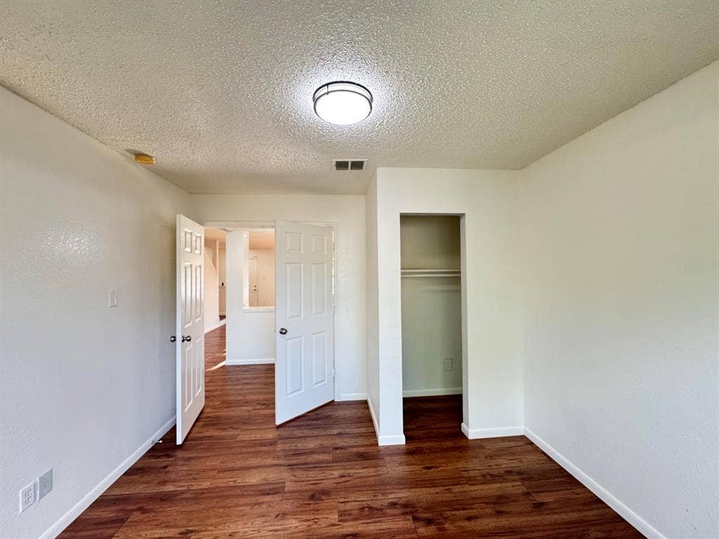 7305 Marsland Lane, Arlington, TX 76001 Interior room featuring wood-finish flooring, white walls, and a recessed closet with a clothes rod