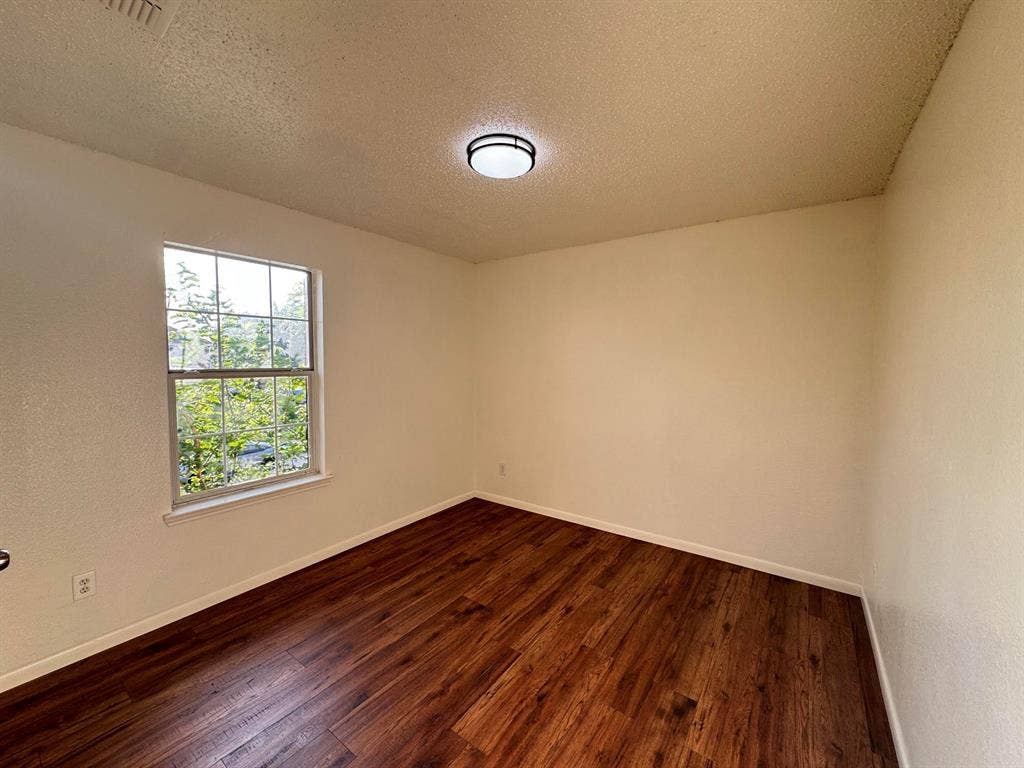 7305 Marsland Lane, Arlington, TX 76001 Bright room featuring wood-finish flooring, a window with exterior greenery, neutral wall tones, white baseboards, and a flush-mount ceiling light