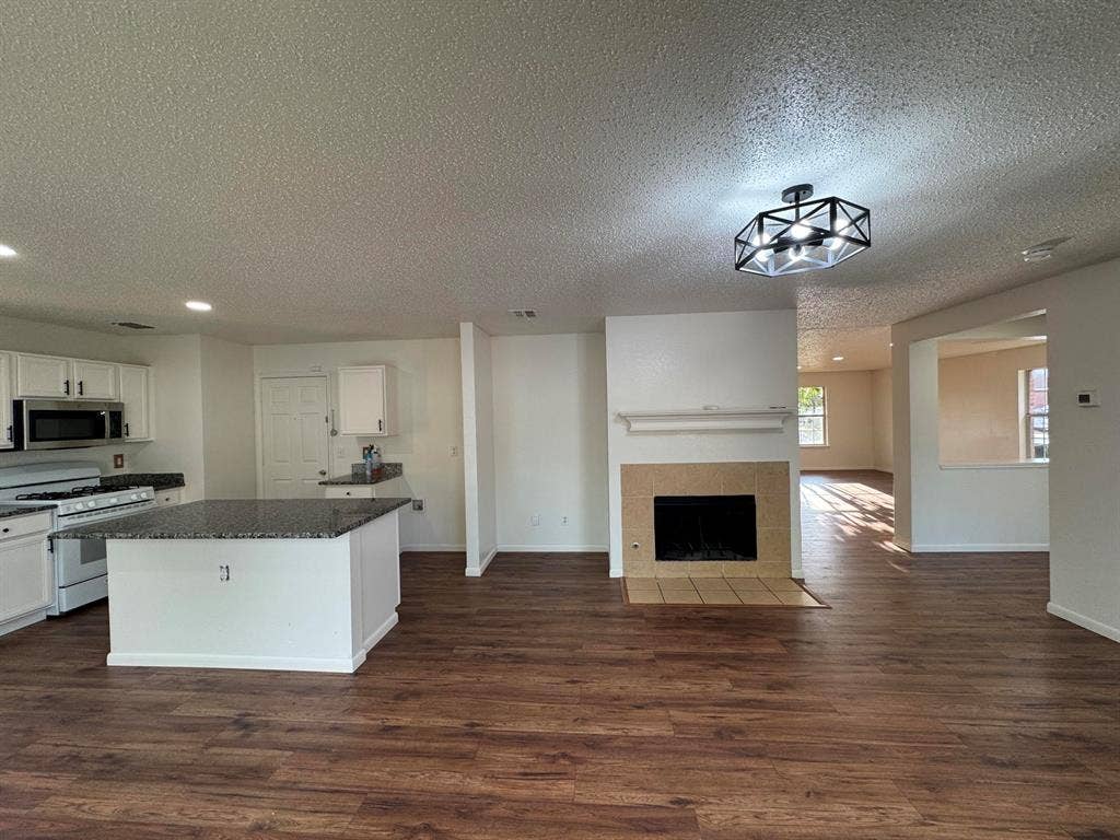 7305 Marsland Lane, Arlington, TX 76001 Open-concept living space with wood-finish flooring, a central kitchen island, and a fireplace with a tile surround
