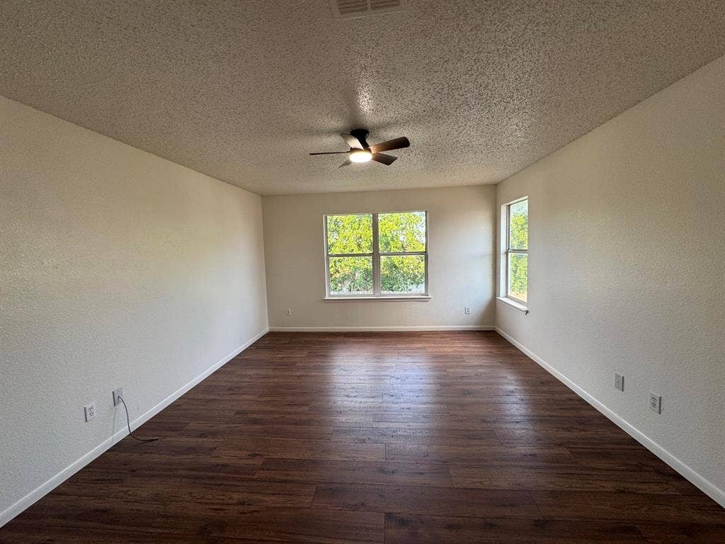 7305 Marsland Lane, Arlington, TX 76001 Spacious room featuring wood-finish flooring, two large windows, a ceiling fan, and white baseboards