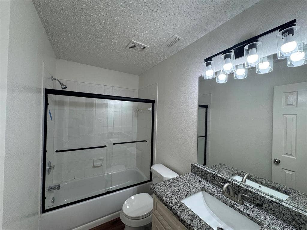 7305 Marsland Lane, Arlington, TX 76001 Modernized bathroom featuring a full tub with sliding glass doors, a granite vanity countertop, and updated overhead lighting
