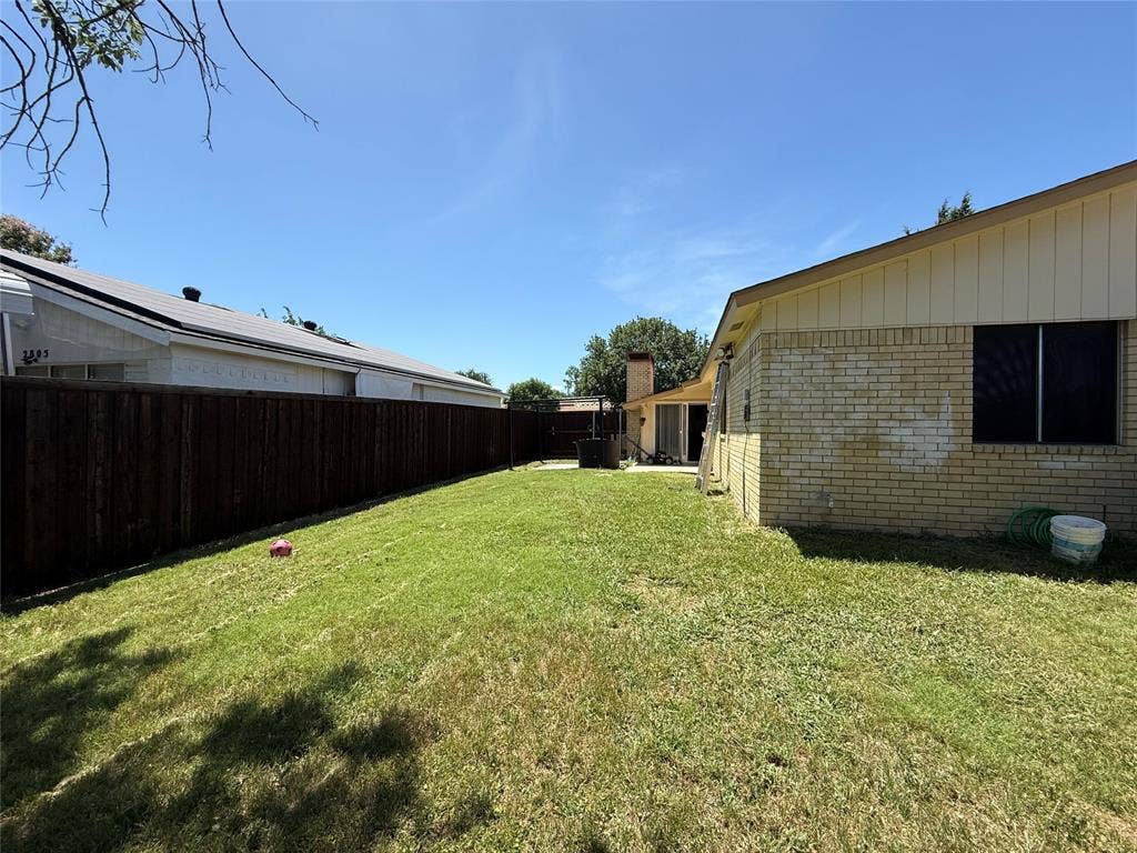 2809 Royalty Drive, Garland, TX 75044 Spacious backyard with a wood privacy fence, featuring a manicured lawn and brick exterior
