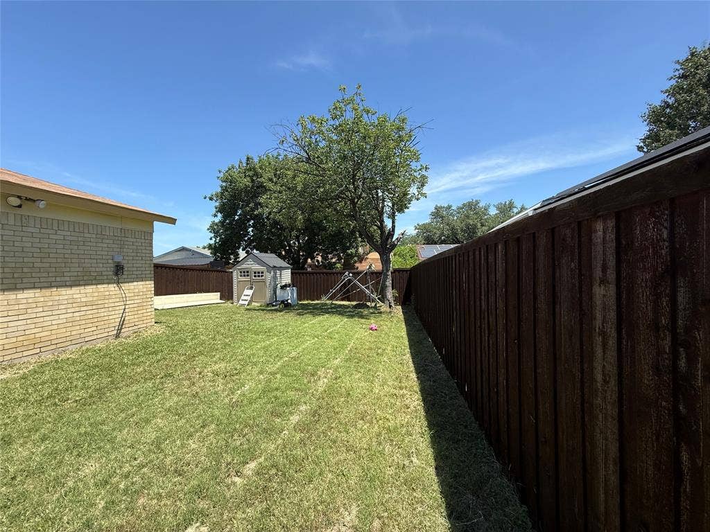 2809 Royalty Drive, Garland, TX 75044 Expansive yard featuring a wooden privacy fence, mature trees, and a storage shed