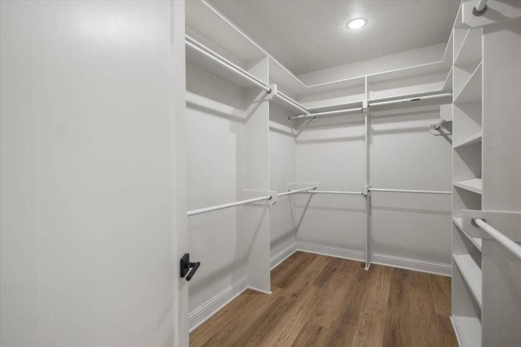 Walk-in closet featuring wood-finish flooring, recessed lighting, multiple shelving units, and hanging rods