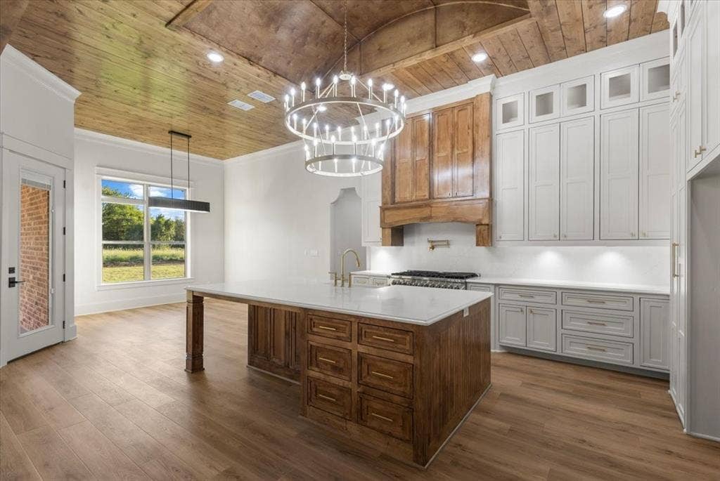 Vaulted wood-finish ceiling, central island with seating, extensive white cabinetry, wood-finish flooring, and a large window