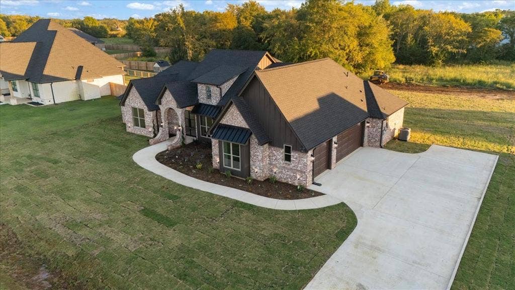 Exterior showcasing a brick and siding facade, arched entryway, dark shingles, an attached garage with wood-finish doors, and a concrete driveway