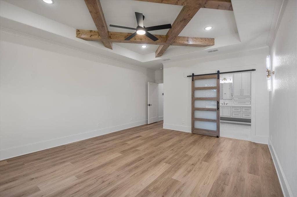 Wood-finish flooring, tray ceiling with wood beams, recessed lighting, and a barn door with frosted glass panels