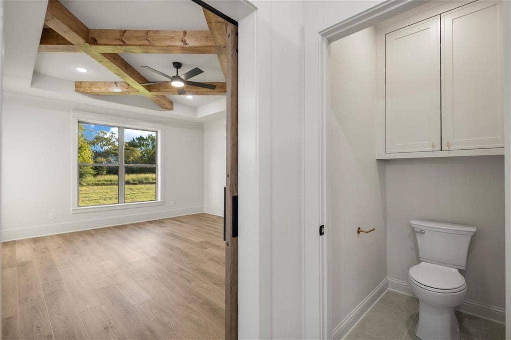 Tray ceiling with wood beam accents, wood-finish flooring, ceiling fan, and a large window