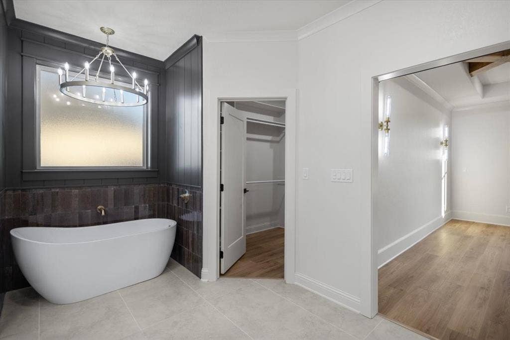 Freestanding bathtub with a bronze-finish faucet, dark wood wall paneling, and a contemporary chandelier