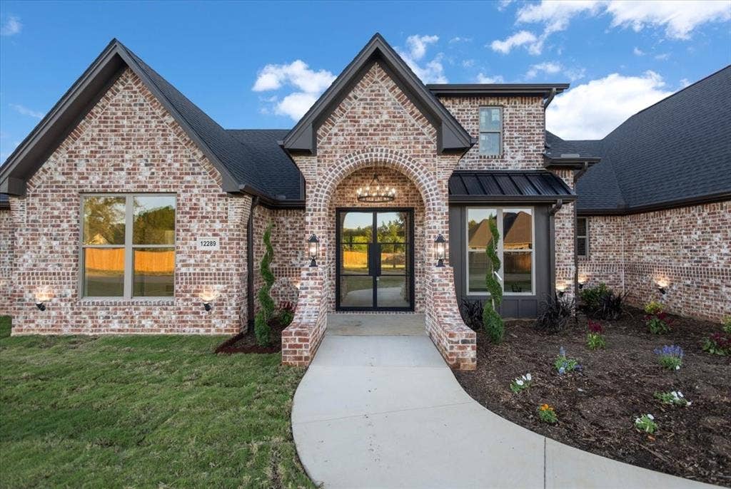 Brick exterior with dark gray roof, arched entry, double glass-paneled front doors, and a concrete pathway