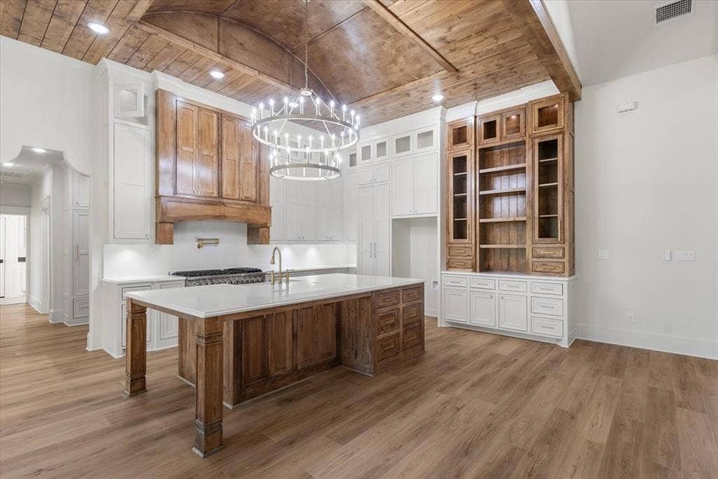 Vaulted wood-paneled ceiling with recessed lighting, large kitchen island with a light-toned countertop, wood-finish flooring, wood cabinetry, and a built-in shelving unit