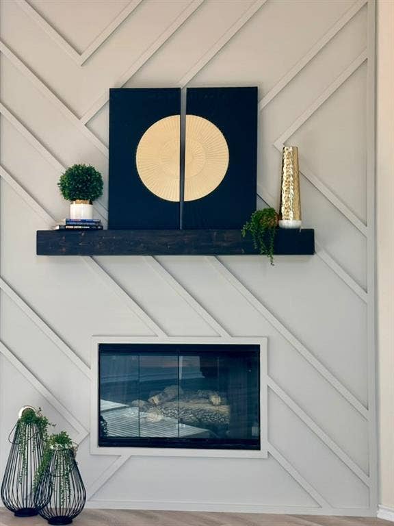 Fireplace accent wall featuring a geometric lattice molding design, dark-stained timber mantel, and glass-front fireplace insert