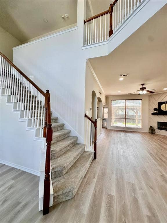 Two-story foyer featuring a staircase with wood-finish handrails and white balusters, wood-finish flooring, and a fireplace with decorative wall paneling