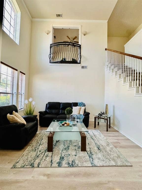 Double-height ceilings featuring large windows, a wrought-iron decorative balcony, and a staircase with white balusters and a wood-finish handrail