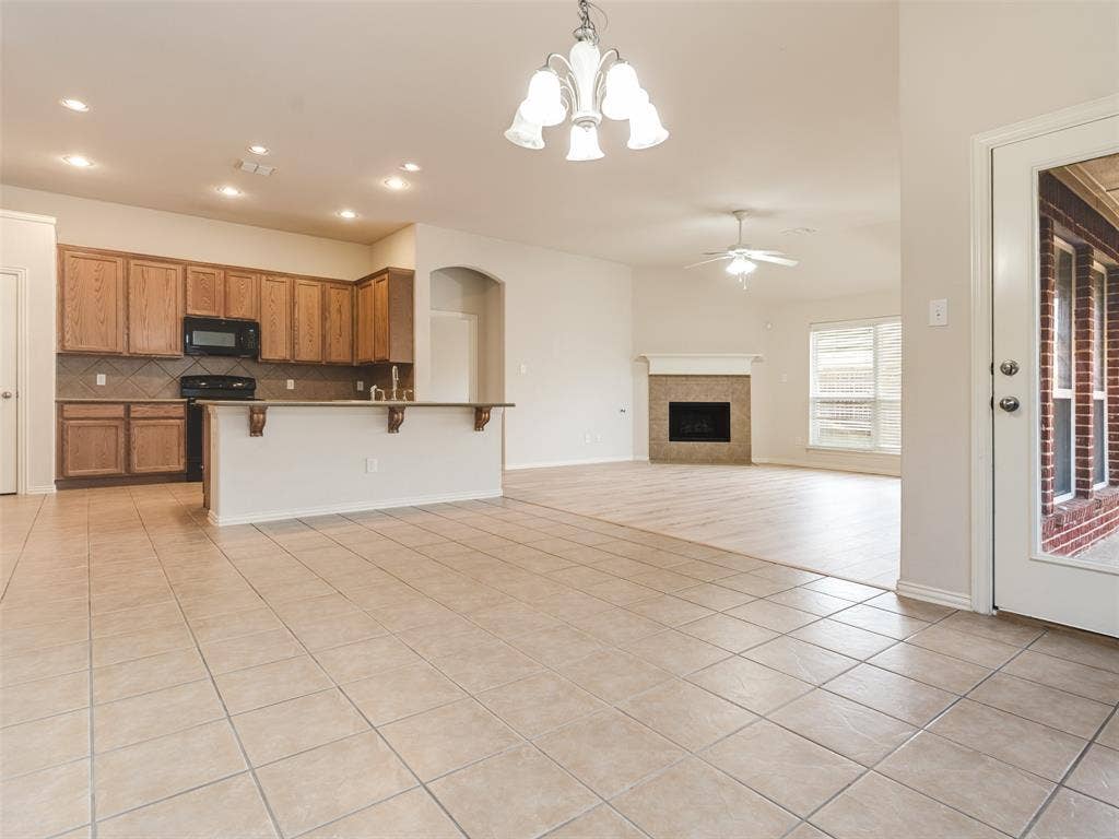 Open-concept area featuring tile flooring, a kitchen with wood cabinetry and a breakfast bar, recessed lighting, and a brick-surround fireplace