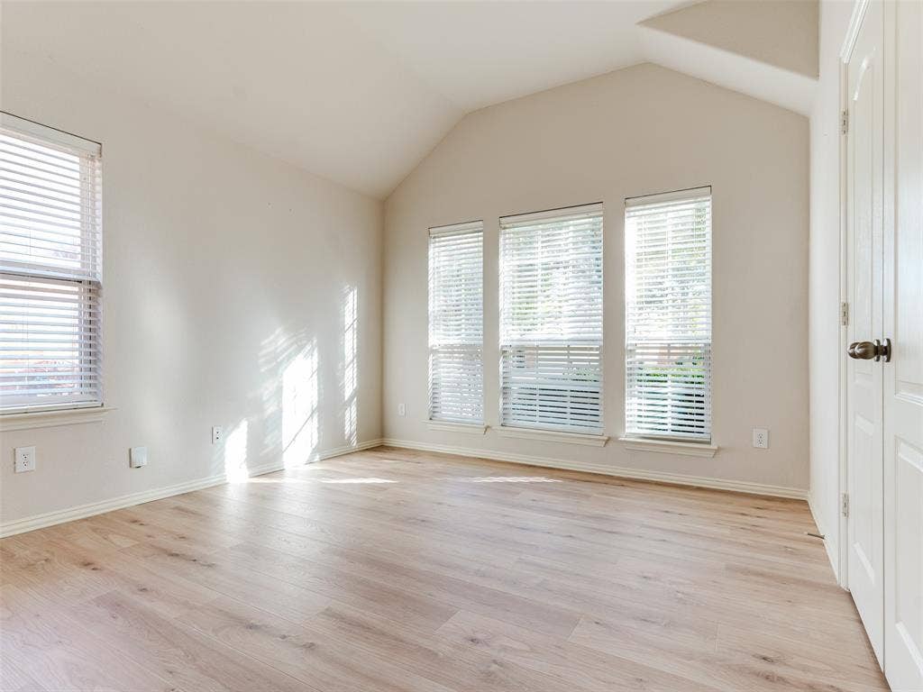 Vaulted ceilings, wood-finish flooring, and multiple tall windows with horizontal blinds