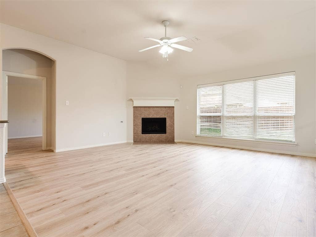 Living area featuring wood-finish flooring, a corner fireplace with tile surround, vaulted ceilings with a ceiling fan, and large windows with horizontal blinds